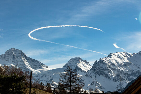 Curved Chemtrail above snowy mountains Swiss Alps Switzerland
