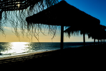 Serene vacation beach setting during a sunset with silhouetted sunshades