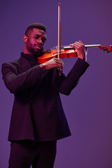 Elegant musician in black suit playing violin on vibrant purple background in artistic performance concept