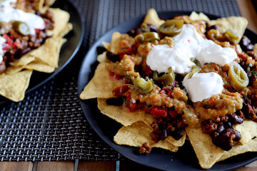 Appetizing dish on a plate: corn chips nachos with fried minced meat and guacamole, salsa, jalapeno top view. Homemade Mexican cuisine.