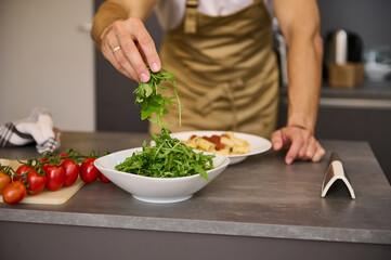 Close-up chef hands holding fresh arugula leaves, garnishing meal, cooking Italian spaghetti in the home kitchen.