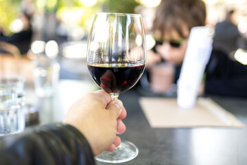 Hand holding a glass of red wine on a table in a restaurant.