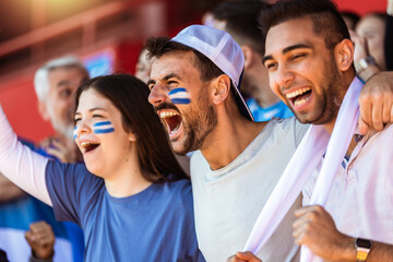 Sport fans cheering at the game on stadium. Wearing blue and white colors to support their team....