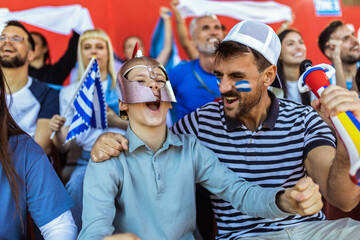 Greece fans cheering at the game on stadium. Wearing blue and white colors to support their team. Celebrating with flags and scarfs.