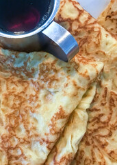 Crepes folded on a plate with a silver pitcher of maple syrup