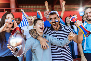 Greece fans cheering at the game on stadium. Wearing blue and white colors to support their team. Celebrating with flags and scarfs. - 790182240
