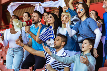 Greece fans cheering at the game on stadium. Wearing blue and white colors to support their team. Celebrating with flags and scarfs. - 790182613