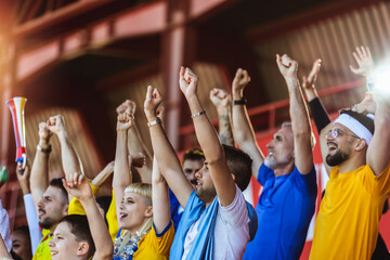 Closeup of hands in the air. Sport fans cheering at the game on stadium. Wearing yellow and blue...