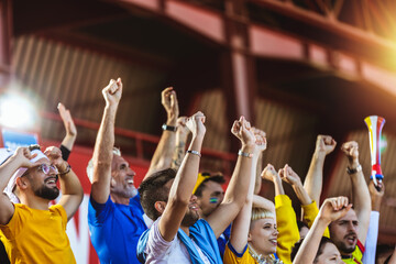 Closeup of hands in the air. Sport fans cheering at the game on stadium. Wearing yellow and blue colors to support their team. Celebrating with flags and scarfs.