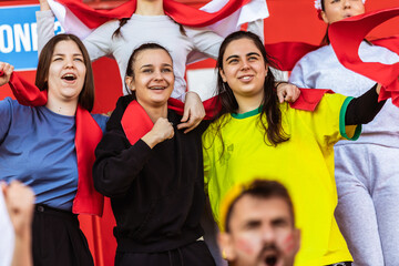 Sport fans cheering at the game on stadium. Wearing red, white and yellow colors to support their team. Celebrating with flags and scarfs.