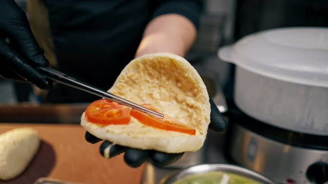 close-up of a chef in black gloves putting pies tomato bun with a spoon