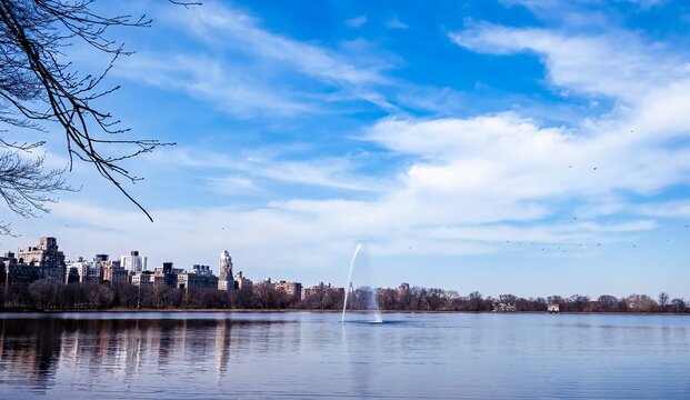Jacqueline Kennedy Onassis Reservoir, Central Park, New York City, New York. Lake on a beautiful early spring day with blue sky and wispy clouds, fountain in the center. Popular jogging spot.