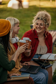 Three happy female students cheering with a coffee to go while sitting in a campus outdoors