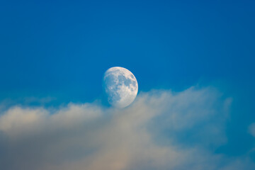 Shining moon in a blue sky with white clouds.