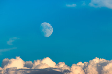 Shining moon in blue sky above cumulus clouds