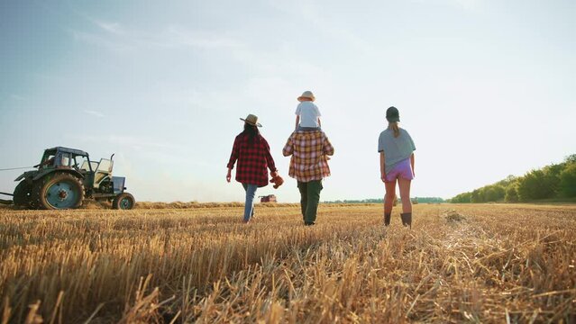 Family walking on wheat field at sunset. Happy parents children holding hands talking together in summer vacations. Farmers having fun together on farm. Farming lifestyle, vacation, family concept.