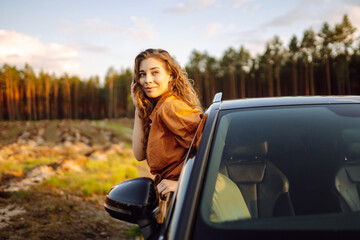 Young woman sitting in car and leaning on window during her road trip and enjoying beautiful  day...