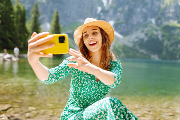 Happy woman with a mobile phone, takes a selfie, communicates via video link with lake views in the...