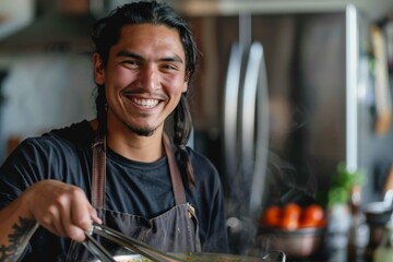 Male chef with tattoos laughing while stirring a dish in a bustling kitchen setting