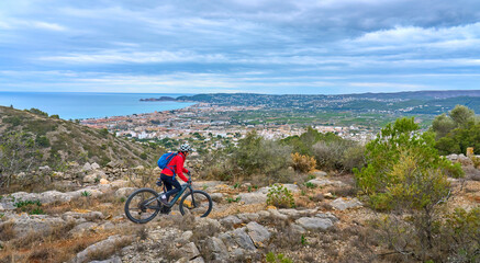activ senior woman riding her electric mountain bike on the cliffs above the city of Denia, Costa...