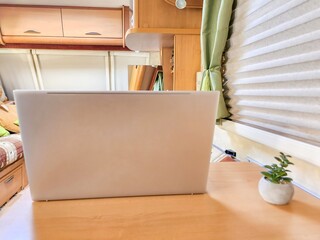 Laptop on the table in cozy camper van with a soft green plant for decor, creating a peaceful work...