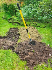 A yellow shovel with a long handle digging soil in a garden. Soil mix of dirt, rocks, and pebbles.  Ideal for promoting landscaping services and inspiring outdoor projects.