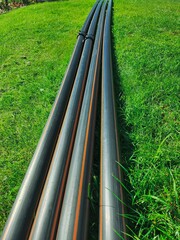 Close-up of four black plastic pipes neatly arranged on lush green grass field under bright sunlight, showcasing contrast between man-made objects and natural environment.