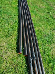 Black Plastic Pipes Arranged Neatly on Lush Green Grass Field, Industrial Equipment for Plumbing...