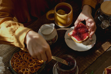 Woman prepares sandwich with berry jam during breakfast on sunny morning.