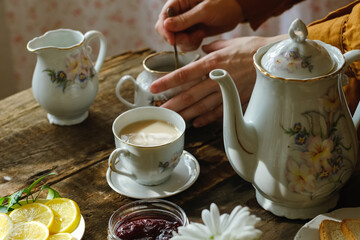 Tea party. Hands adding sugar to cup of tea with milk.