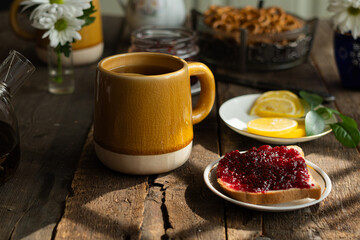 Mug of tea with lemon and toast with jam on wooden table.