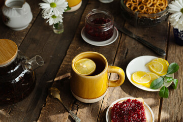 Mug of tea with lemon and toast with jam on wooden table.