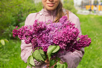The young woman is holding lilacs and walking in the park.