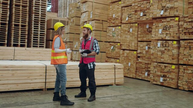 Two construction professionals with hard hats discuss inventory in a timber warehouse.