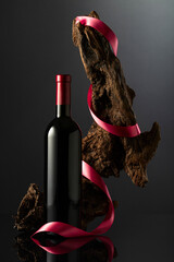 Bottle of red wine and old weathered snag with red satin ribbon.