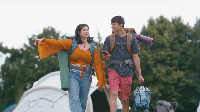 Young couple going to summer music festival arriving at site with camping equipment and mobile phone - shot in slow motion
