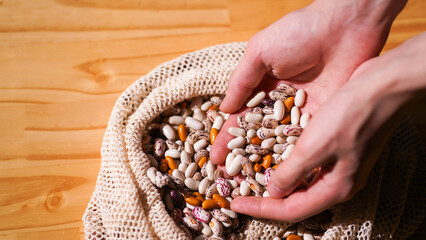 Hands pick through assortment of multicolored beans in crocheted bag on wooden table. Selecting...