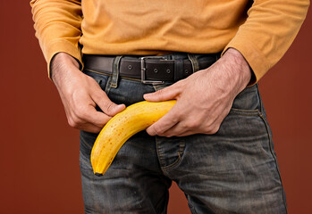 A man in jeans holding a banana between his legs, symbolizing his penis in an flaccid state. Men's health prostate prevention,Erection problem, male health
