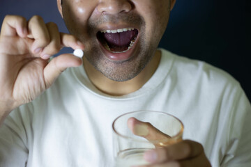 Male hand holding white pills
round and glass of water to take medicine Treat sickness Treat pain...