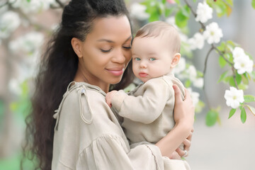Fashion portrait black woman mother holds hugs newborn baby at spring blossom, Mother's Day concept.