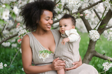 Obraz premium Fashion portrait black woman mother holds hugs newborn baby at spring blossom, Mother's Day concept.