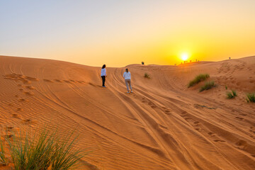Tour groups climb the red sand dunes at Dubai Desert as the sun sets in the distance in Dubai, United Arab Emirates.