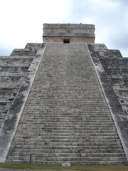 The stairs leading up to the ancient temple of Chichen Itza sit under a cloud sky.