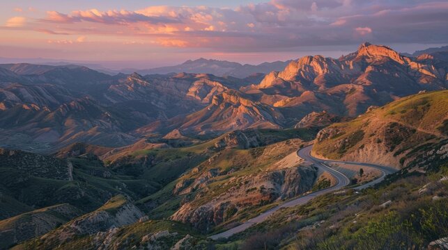A winding mountain road illuminated by the warm glow of sunrise, casting long shadows on the rugged terrain and painting the sky in hues of pink and orange.
