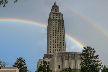The Louisiana State Capitol building with lush green trees, blue sky, clouds and a rainbow in Baton Rouge Louisiana USA