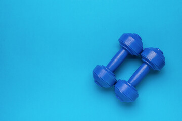 A pair of blue dumbbells on a blue background. - obrazy, fototapety, plakaty