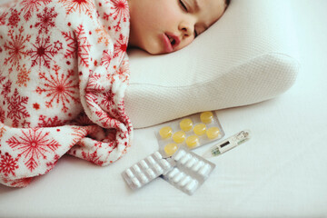 Sick little boy sleeping in white bed with a thermometer and antipyretic tablets on a orthopedic pillow
- 790318235