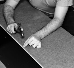 a carpenter furniture maker hammers a nail into the back of the cabinet with a hammer, black and white photo - 790321801