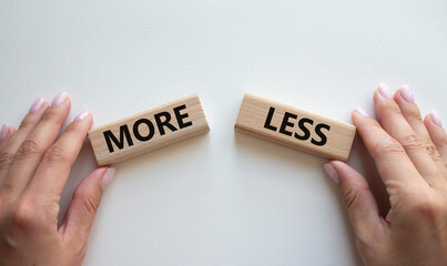 More or Less symbol. Concept word More or Less on wooden blocks. Businessman hand. Beautiful white...