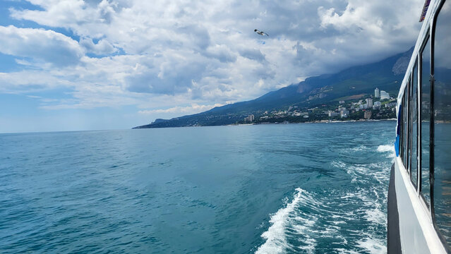 The sky is cloudy, the shore is astern and the blue sea waves.